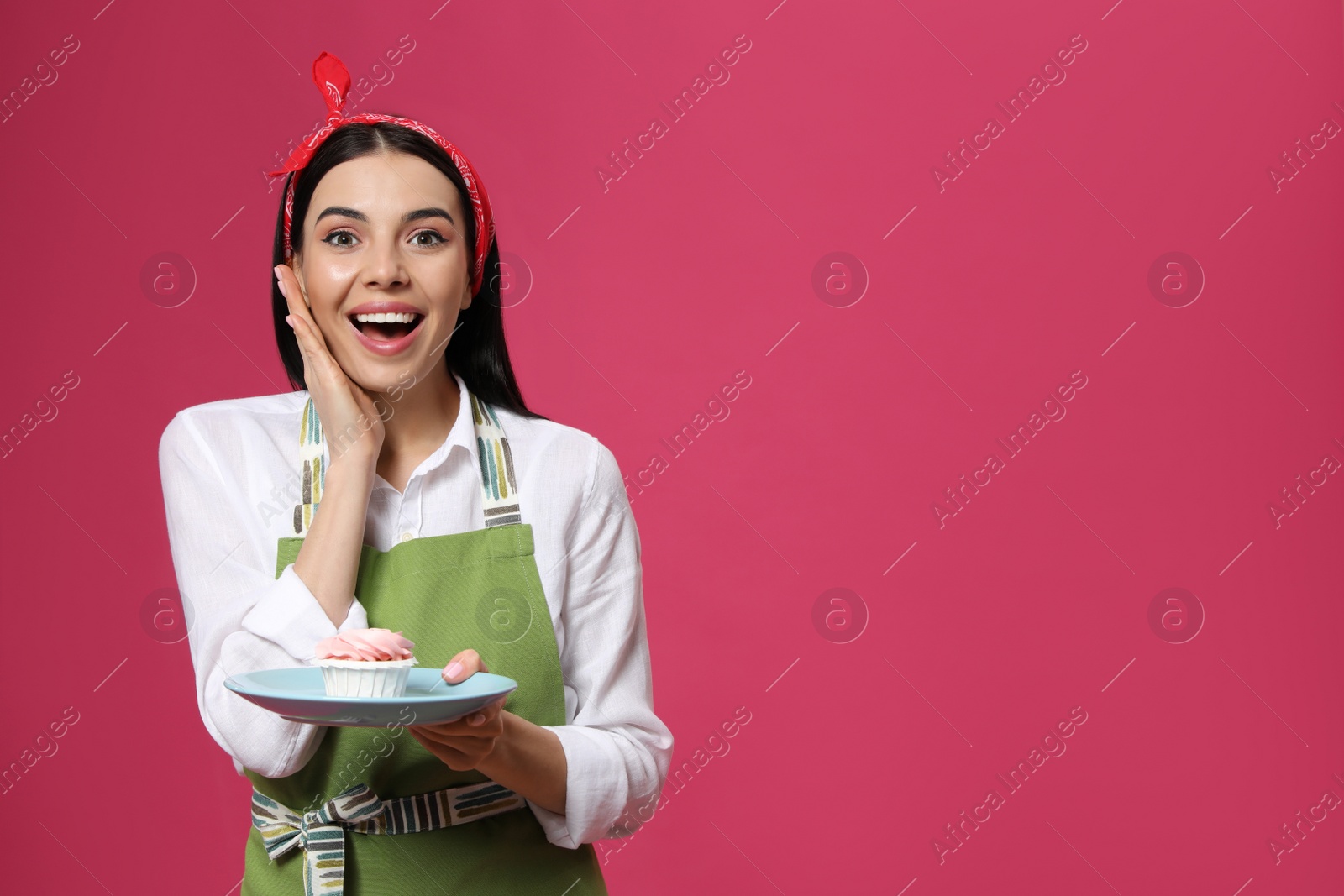 Photo of Emotional housewife with tasty cupcake on pink background, space for text