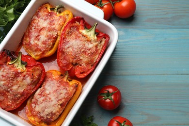 Photo of Tasty stuffed peppers in dish and ingredients on light blue wooden table, flat lay. Space for text