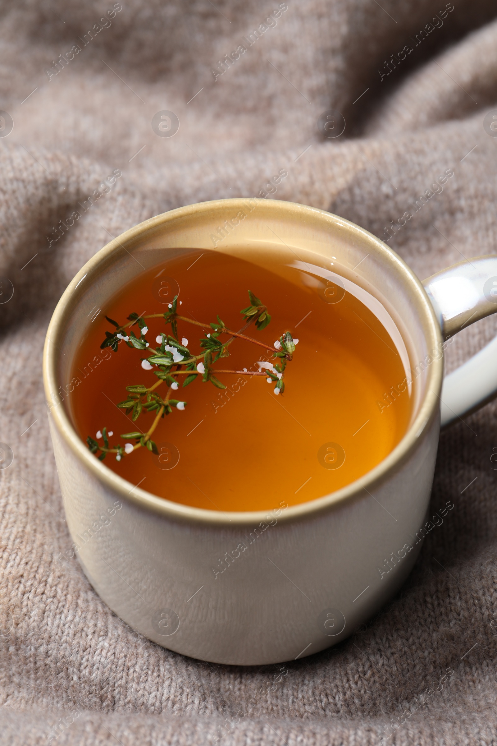 Photo of Cup of aromatic herbal tea with thyme on beige fabric