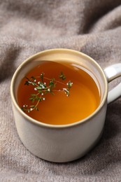 Cup of aromatic herbal tea with thyme on beige fabric
