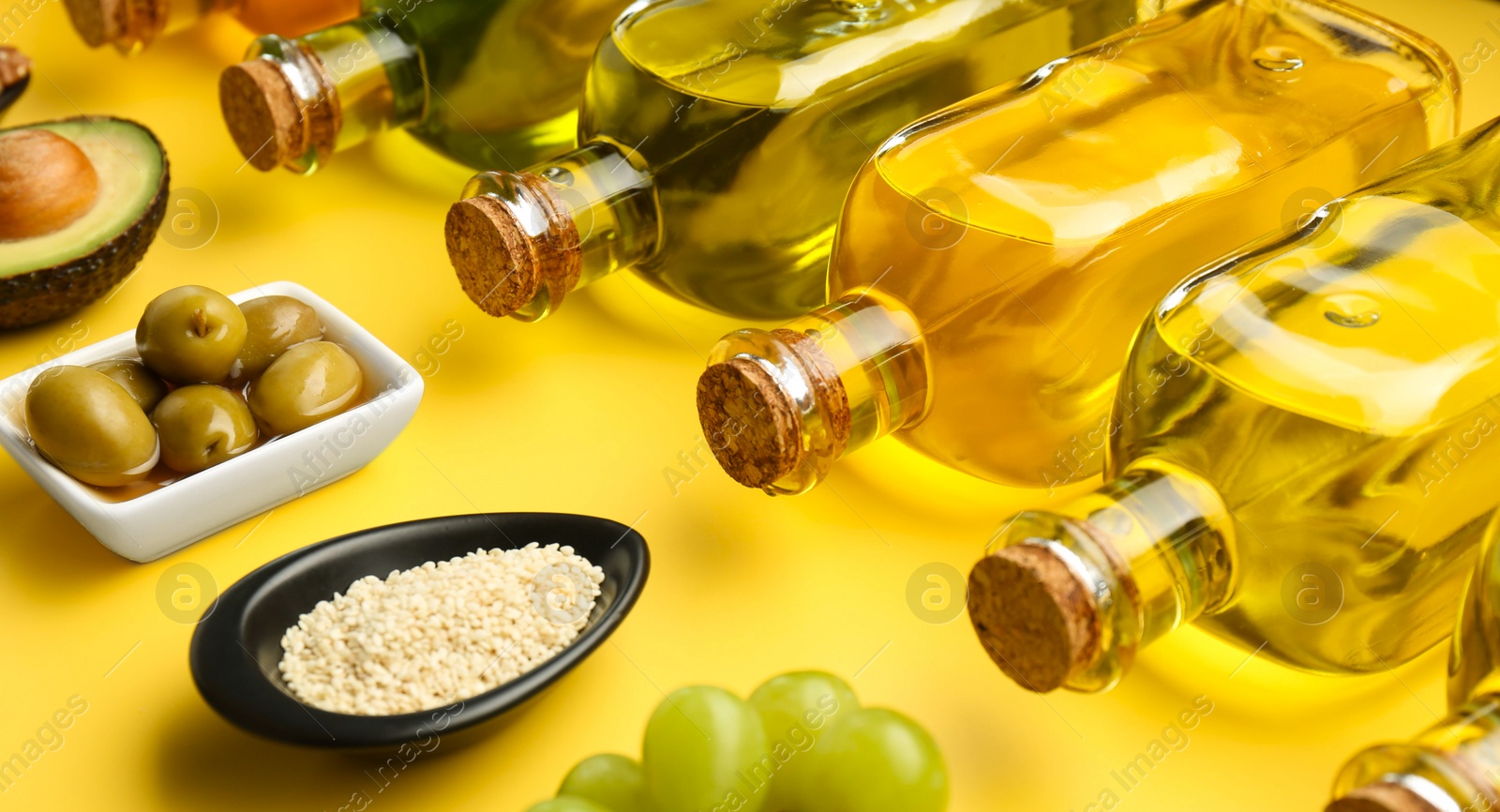 Photo of Vegetable fats. Different oils in glass bottles and ingredients on yellow table, closeup