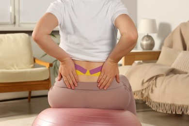 Closeup of pregnant woman with kinesio tapes doing exercises on fitball at home, back view