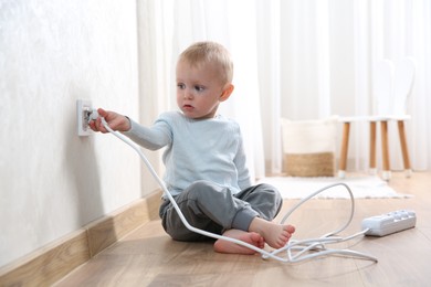 Photo of Little child playing with electrical socket and power strip plug at home. Dangerous situation