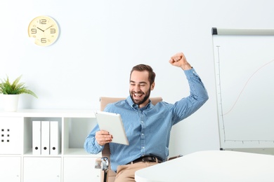 Photo of Emotional young man with tablet celebrating victory in office