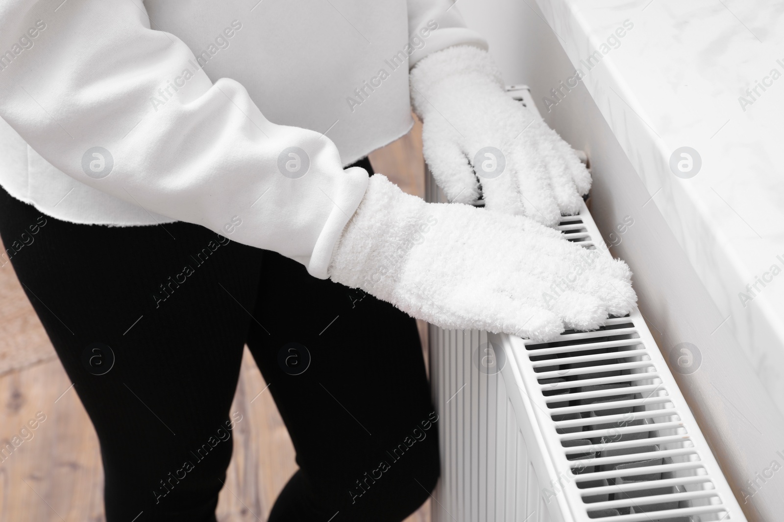 Photo of Girl warming hands on heating radiator indoors, closeup