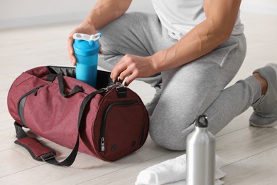 Photo of Young man putting shaker with protein into bag indoors, closeup