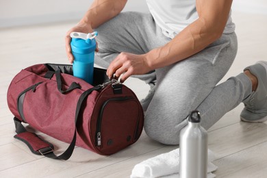 Young man putting shaker with protein into bag indoors, closeup