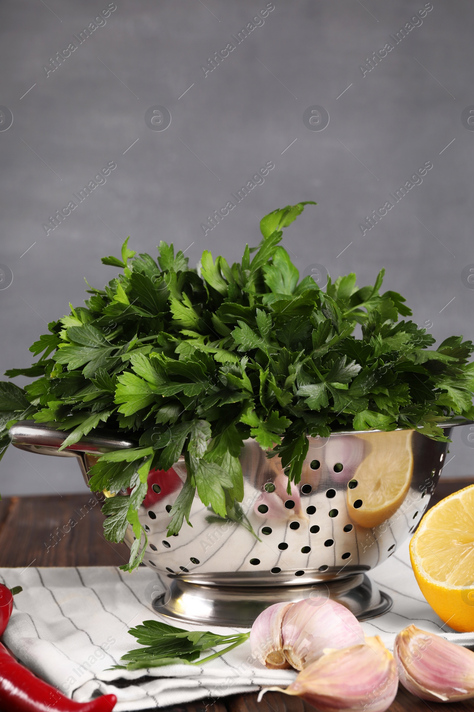 Photo of Colander with fresh parsley, garlic, lemon and chili pepper on wooden table, closeup