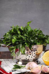 Colander with fresh parsley, garlic, lemon and chili pepper on wooden table, closeup