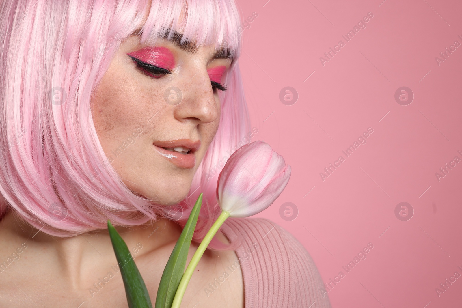 Photo of Beautiful woman with bright makeup, fake freckles and tulip on pink background, closeup. Space for text
