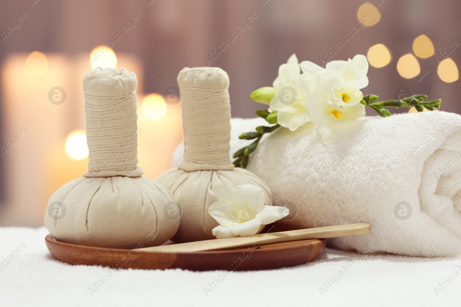 Photo of Beautiful composition with different spa products and flowers on white towel against blurred background, closeup