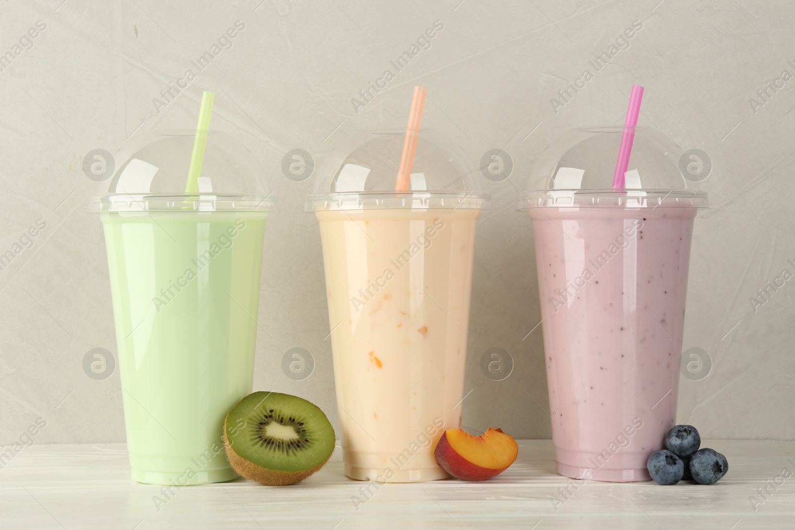 Photo of Plastic cups of different tasty smoothie and fresh fruits on white wooden table