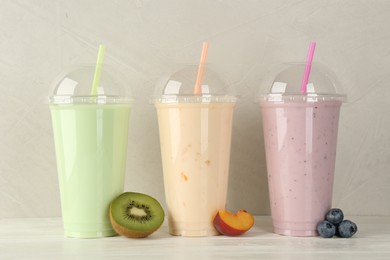 Photo of Plastic cups of different tasty smoothie and fresh fruits on white wooden table