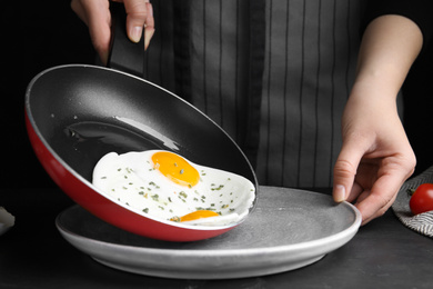 Photo of Woman putting tasty cooked eggs onto plate from frying pan at black table, closeup