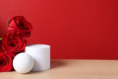 Photo of Stylish presentation for product. Beautiful roses and geometric figures on wooden table against red background, space for text