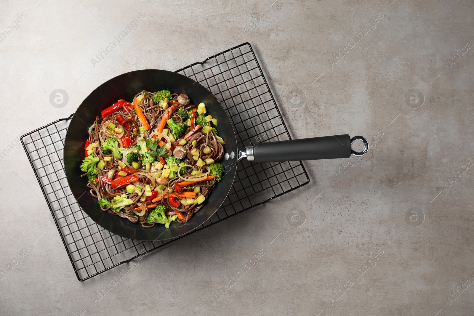 Photo of Stir-fry. Tasty noodles with meat and vegetables in wok on grey textured table, top view