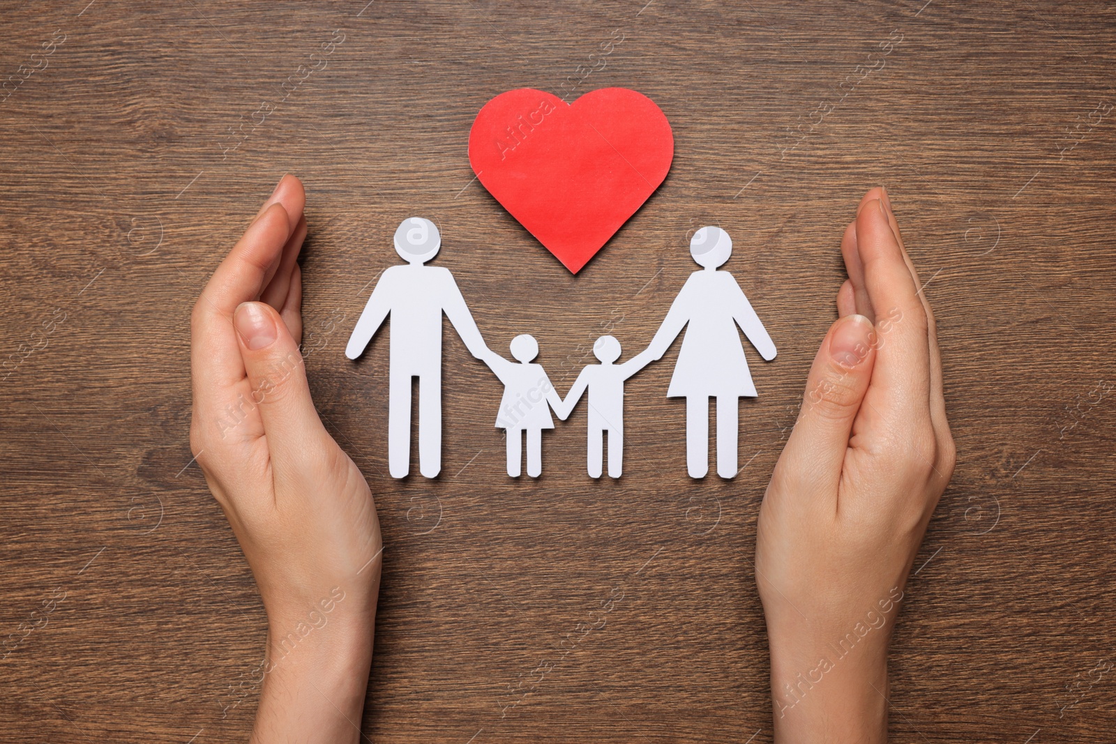 Photo of Woman protecting paper family cutout at wooden table, top view. Insurance concept