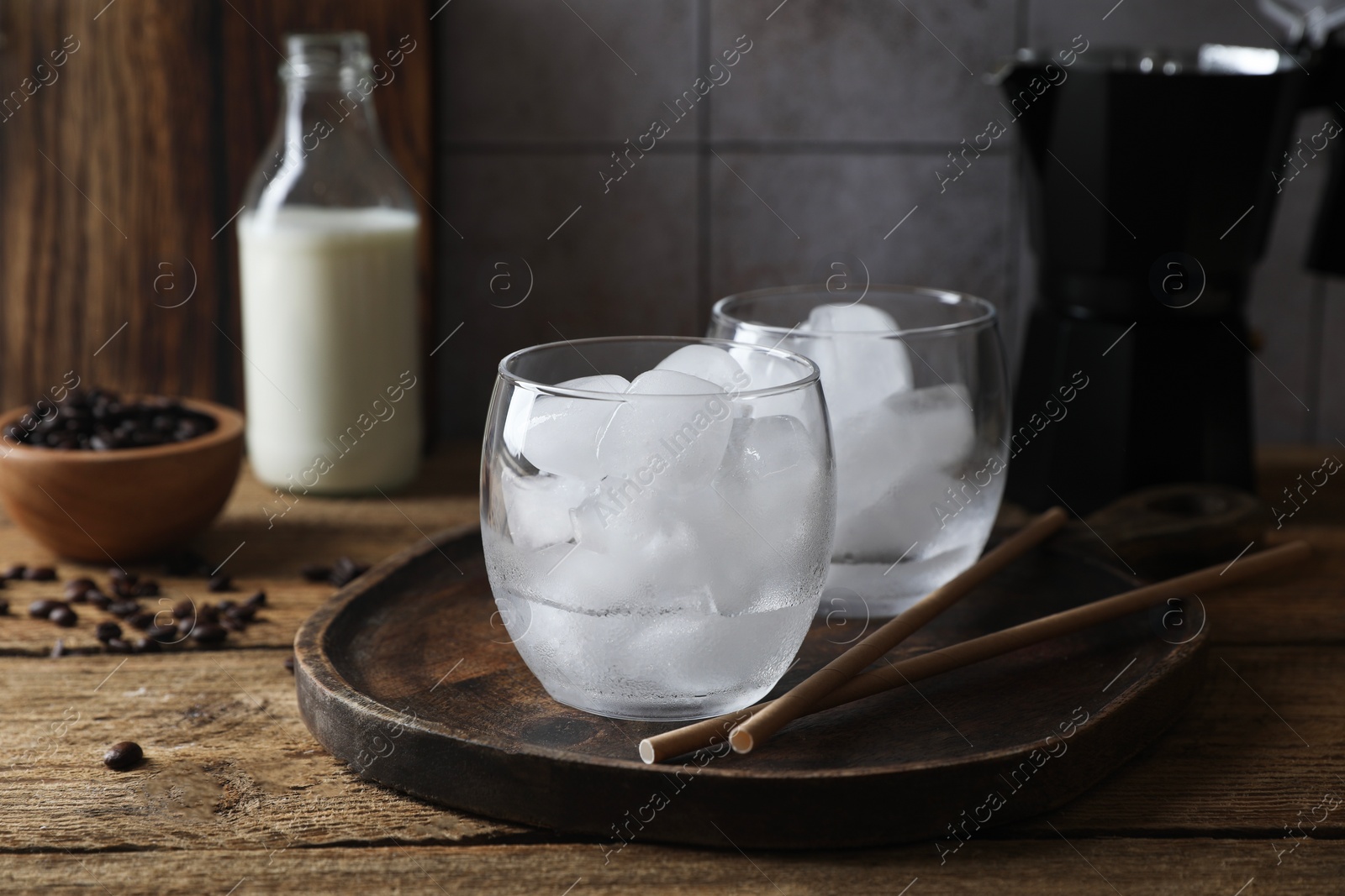 Photo of Making iced coffee. Ice cubes in glasses and straws on wooden table