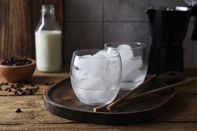 Making iced coffee. Ice cubes in glasses and straws on wooden table