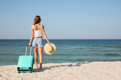 Woman with suitcase on sandy beach near sea, back view