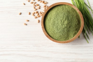 Wheat grass powder in bowl, seeds and fresh sprouts on white wooden table, flat lay. Space for text