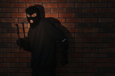 Thief in balaclava with crowbar against red brick wall