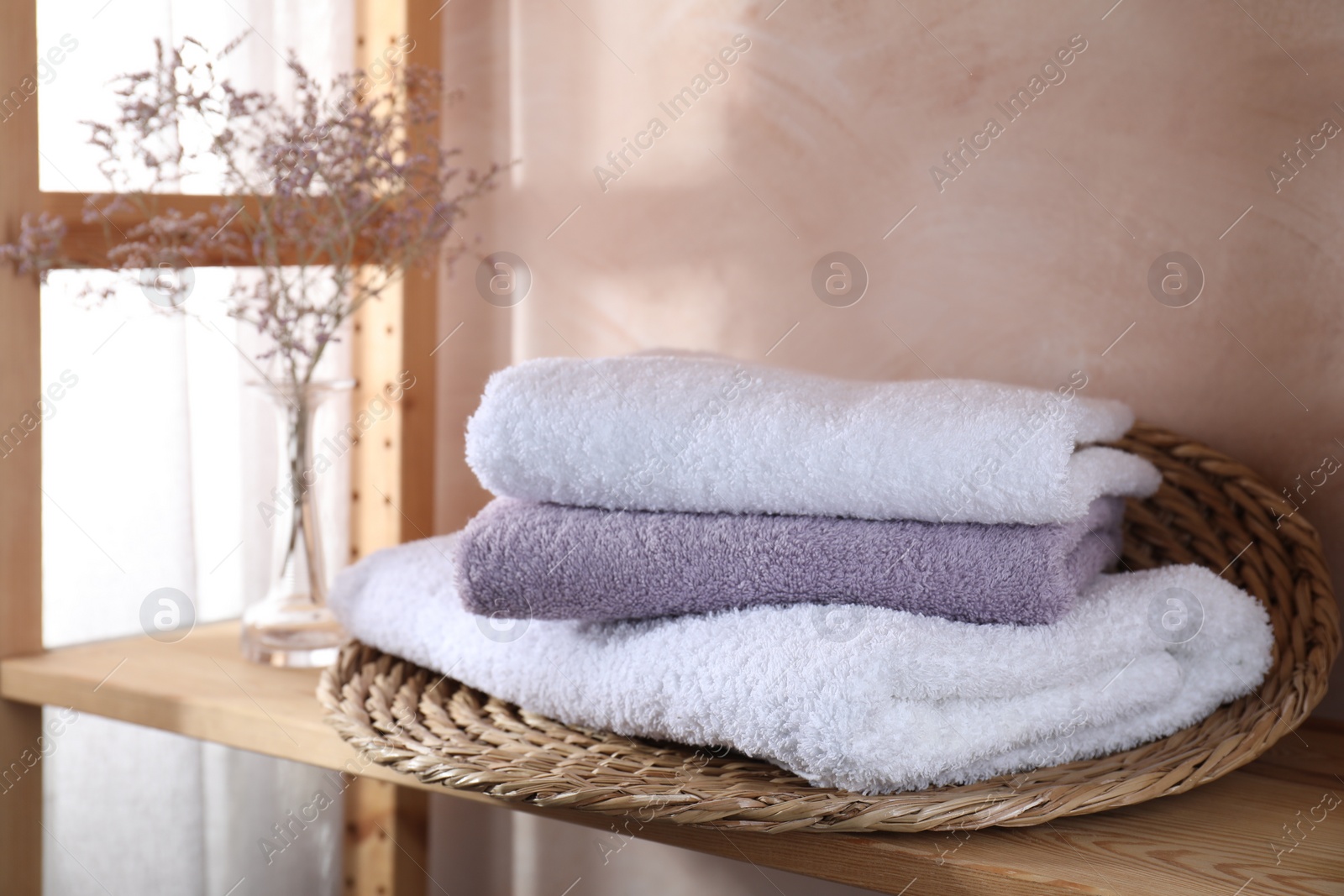 Photo of Stacked soft towels and flowers on wooden shelf indoors