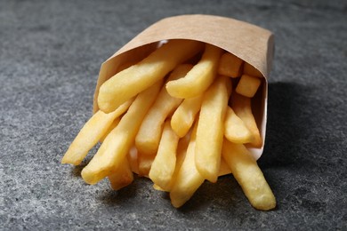 Photo of Delicious french fries in paper box on grey table, closeup