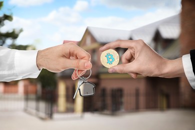 Image of Bitcoin exchange. Man using cryptocurrency to buy house. Seller holding key and buyer with bitcoin outdoors, closeup