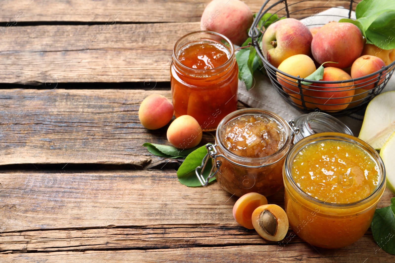 Photo of Jars with different jams and fresh fruits on wooden table. Space for text