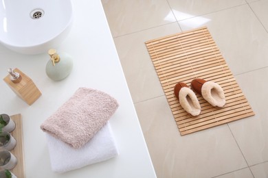 Photo of Wooden mat with slippers on floor in bathroom