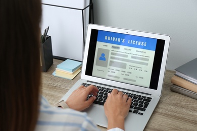 Photo of Woman using laptop to fill driver's license application form at table in office, closeup