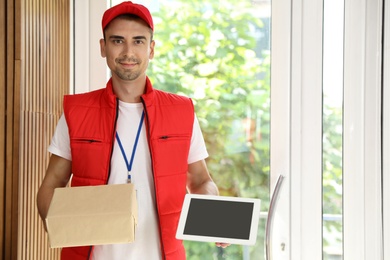 Photo of Happy young courier with parcel and tablet in doorway. Space for text