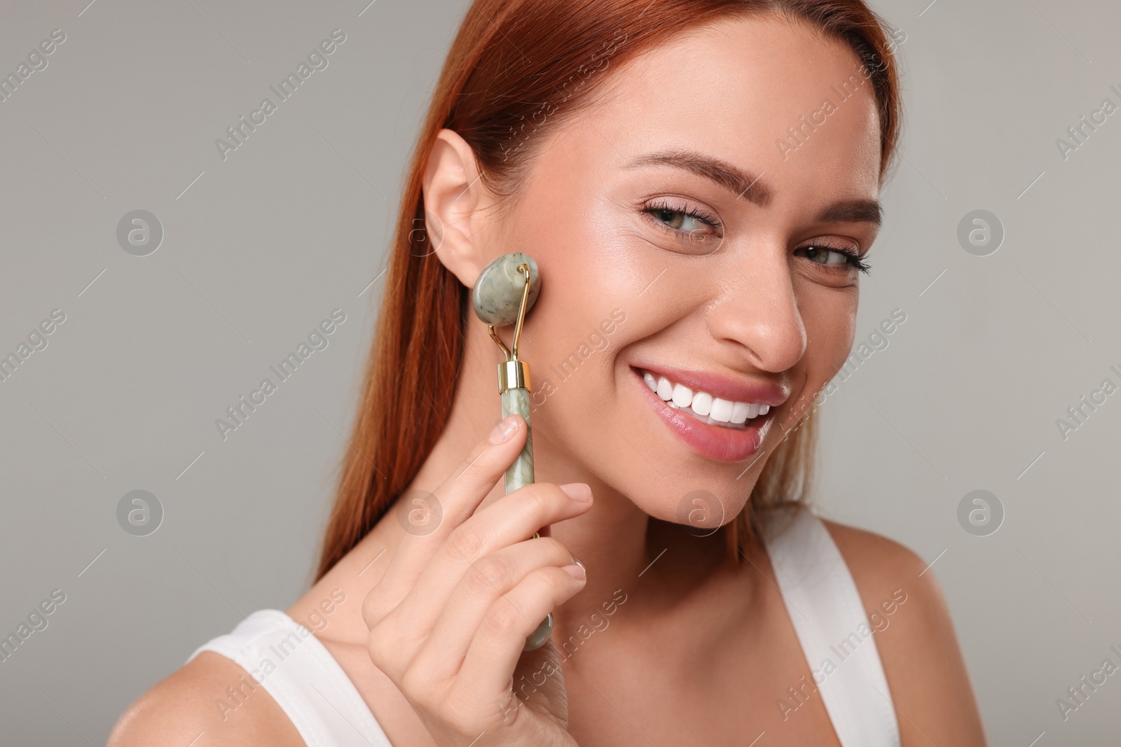 Photo of Young woman massaging her face with jade roller on grey background