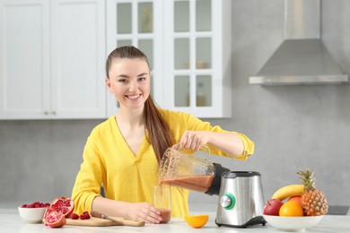 Woman pouring tasty smoothie into glass at white table in kitchen