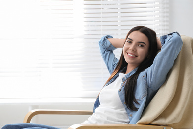 Photo of Young woman relaxing in armchair near window at home