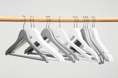 Photo of Empty clothes hangers on wooden rail against light background