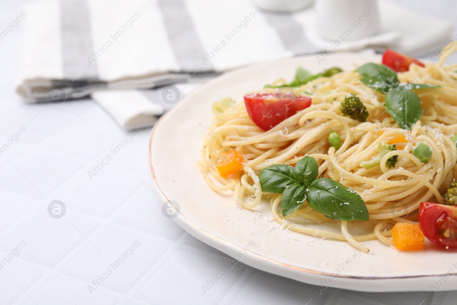 Photo of Delicious pasta primavera with tomatoes, basil and broccoli on white tiled table, closeup. Space for text