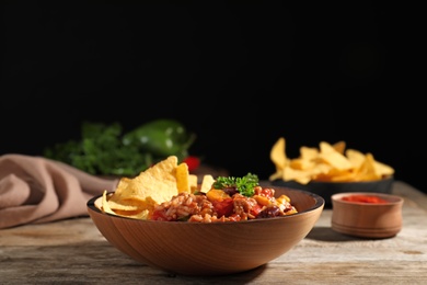 Photo of Tasty chili con carne served with tortilla chips in bowl on table