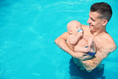 Man with his little baby in swimming pool on sunny day, outdoors