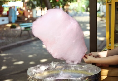 Photo of Woman making cotton candy using modern machine outdoors, closeup