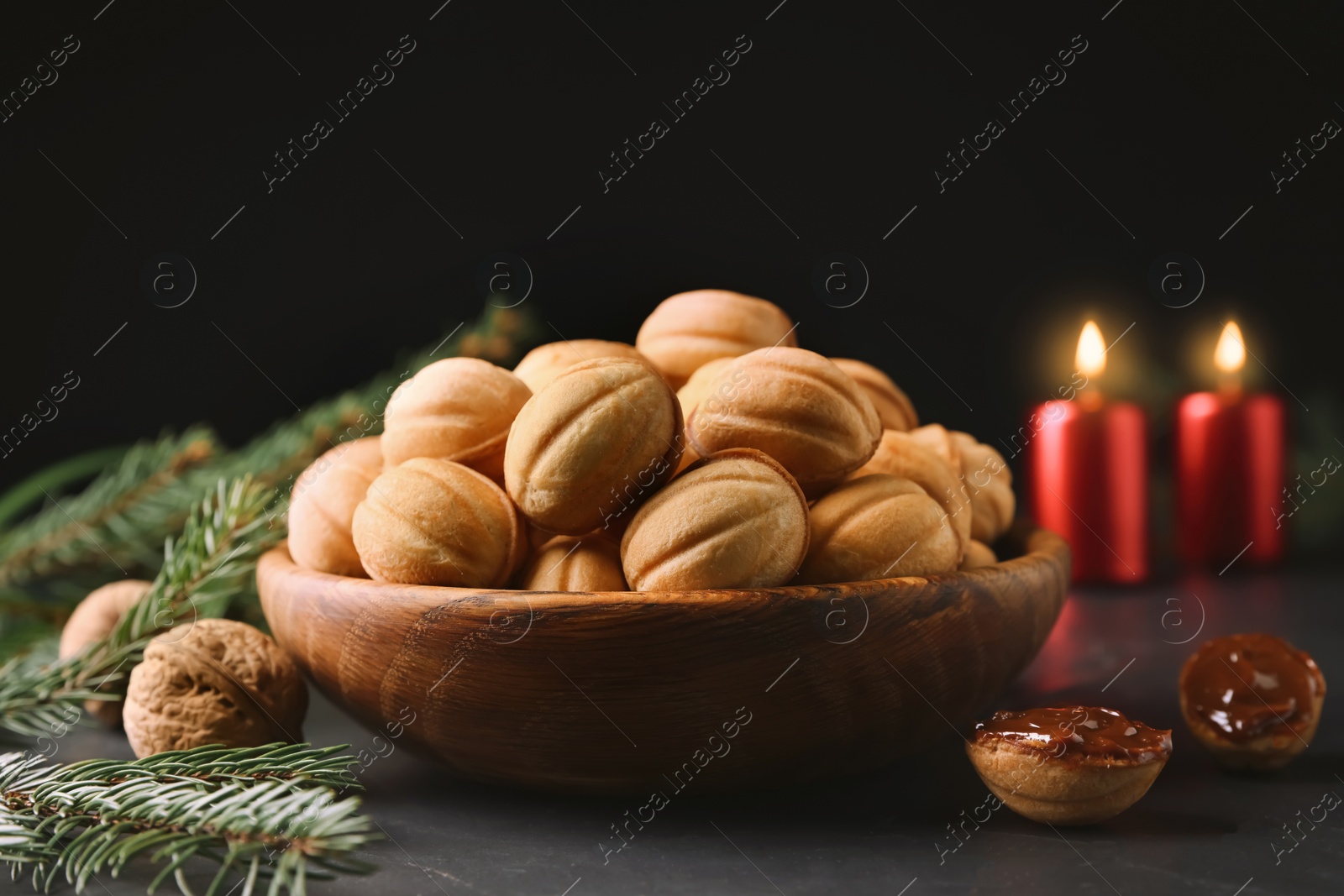 Photo of Homemade walnut shaped cookies with boiled condensed milk, candles and fir branches on black table