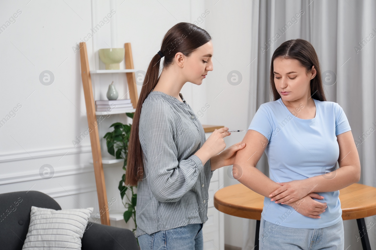 Photo of Woman giving insulin injection to her diabetic friend at home