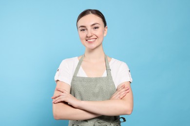 Beautiful young woman in clean apron with pattern on light blue background