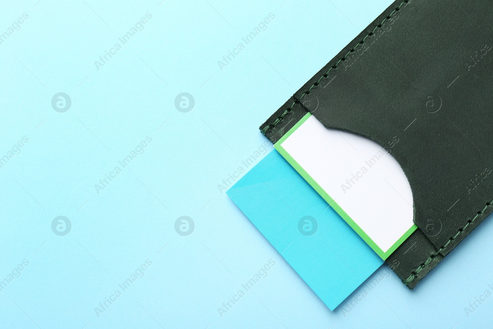 Photo of Leather business card holder with colorful cards on light blue background, top view. Space for text