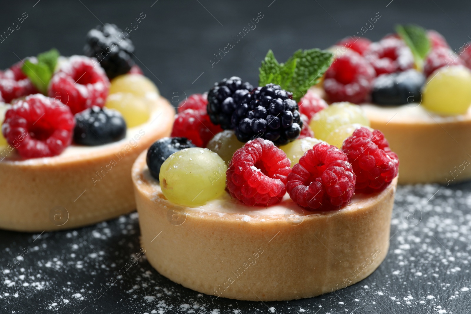 Photo of Delicious tartlets with berries on black table, closeup