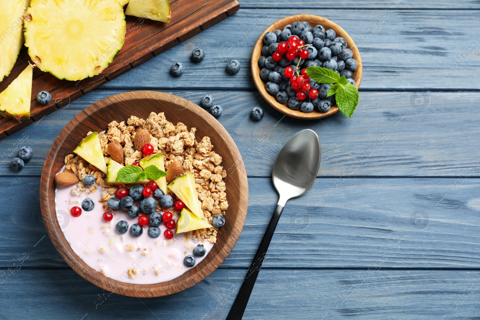 Image of Tasty granola with yogurt, berries and sliced pineapple served for breakfast on blue wooden table, flat lay