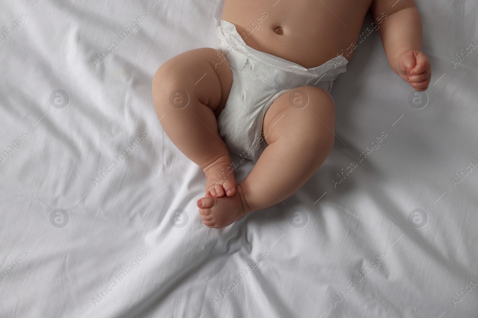 Photo of Little baby in diaper lying on bed, top view