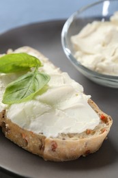Photo of Piece of bread with cream cheese and basil leaves on gray plate, closeup