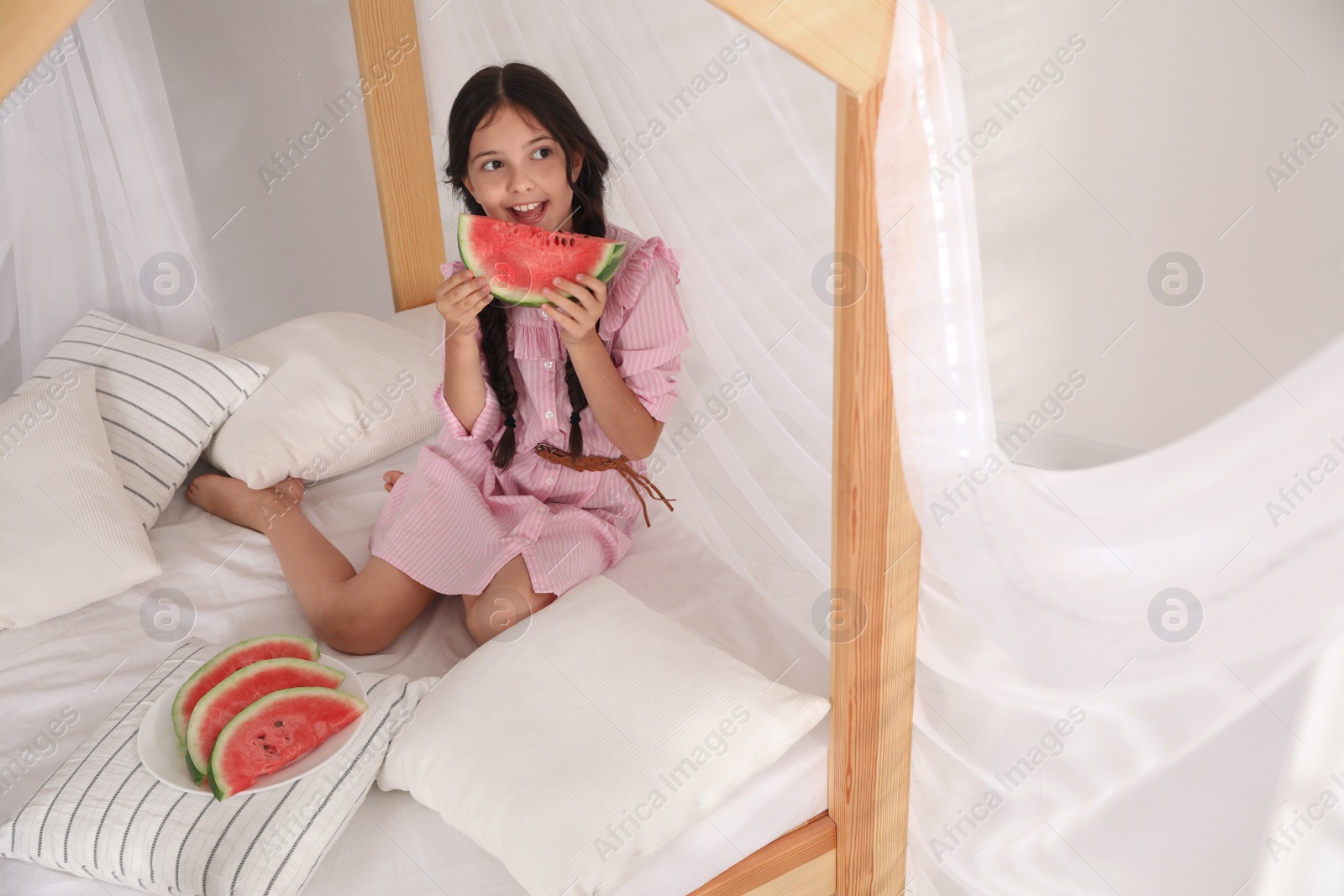 Photo of Cute little girl with watermelon on bed at home